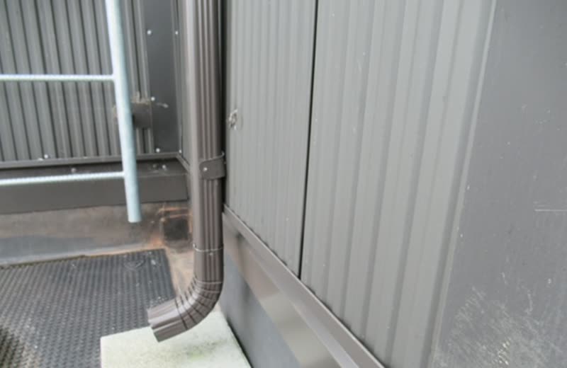 A downspout and its discharge point at the base of the building
